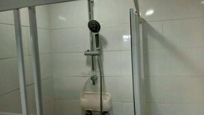 A shower with a handheld showerhead, a handheld soap dispenser, and a wall-mounted faucet.