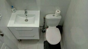 A small, compact bathroom with a white sink, a toilet, and a black floor mat.