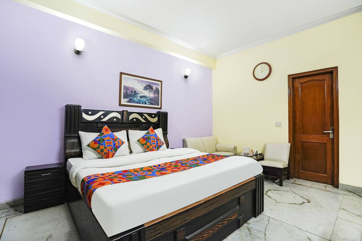 A bedroom with a bed, nightstands, a chair, a wooden door, and a wall clock.