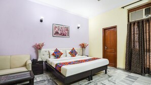 A bedroom with a bed, a sofa, a nightstand, a vase with flowers, a picture on the wall, and a door with curtains. - FabHotel Ivy Inn - Nr ISKCON Temple Noida Sec 35 (Noida)