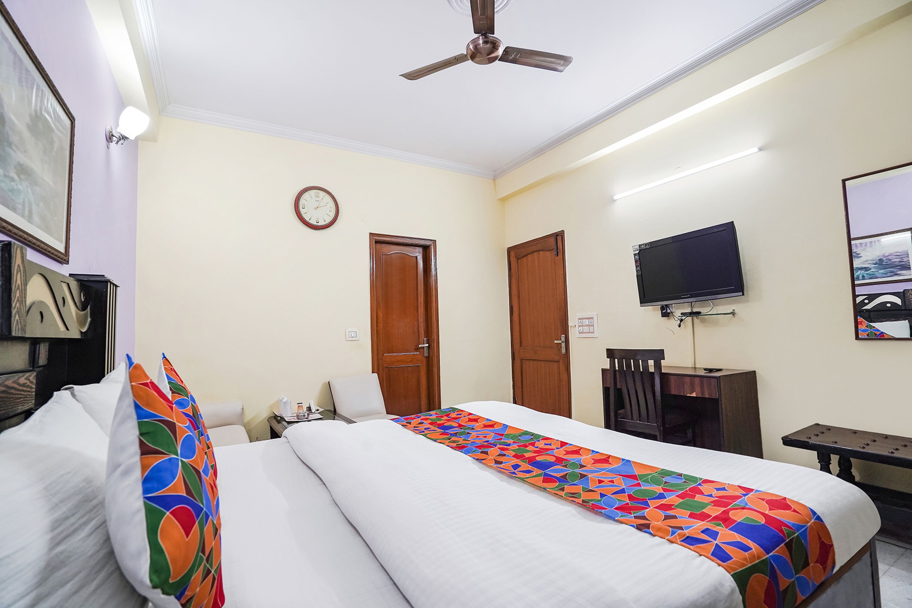 A hotel room with two beds, a desk, a chair, a television, and a ceiling fan.