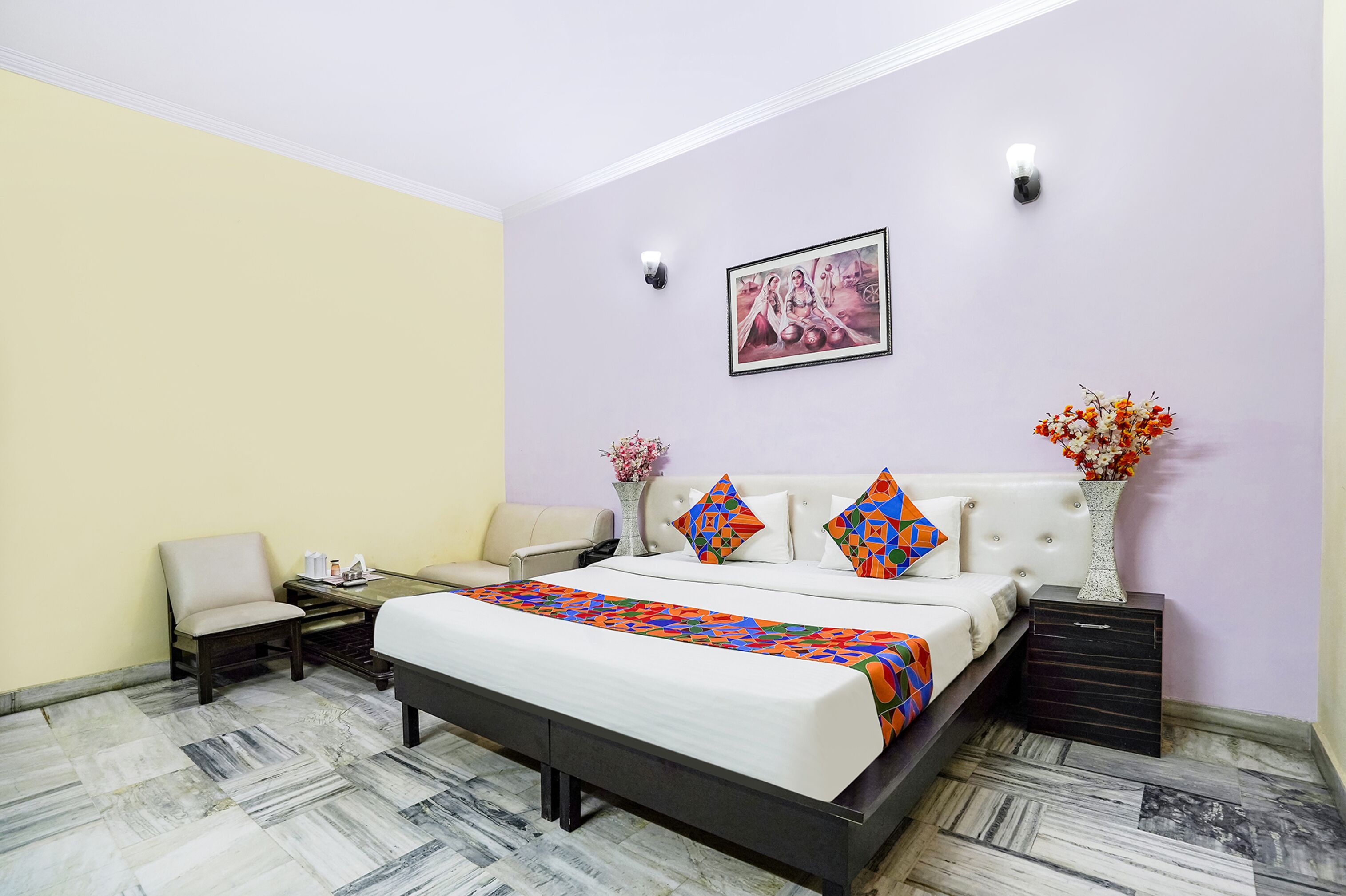 Un dormitorio ordenado con cama, mesitas de noche, una silla y un cuadro decorativo en la pared.