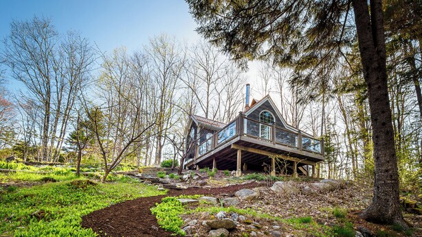 A rustic cabin with a wooden deck and large windows, surrounded by a forested landscape. - A Quiet Riverside Cottage with 2 Fireplaces (Crousetown)