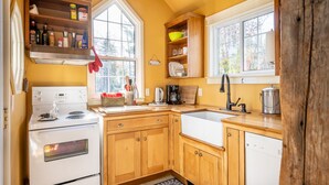 A kitchen with wooden cabinets, a white stove, a sink, and a window. - A Quiet Riverside Cottage with 2 Fireplaces (Crousetown)