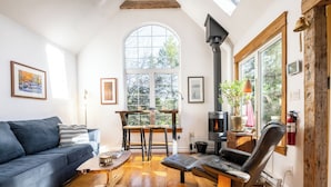 A cozy living room with a sofa, a leather chair, a wooden coffee table, and a large window with a view of trees. - A Quiet Riverside Cottage with 2 Fireplaces (Crousetown)