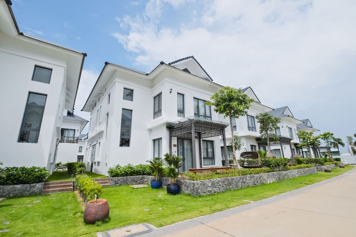 A modern residential building with a well-maintained lawn, stone retaining walls, and a clear sky.
