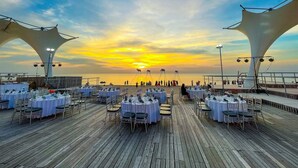 A wooden deck with round tables set for dining, overlooking a sunset over the ocean. - Sunset Sanato Resort & Villas (Phu Quoc)