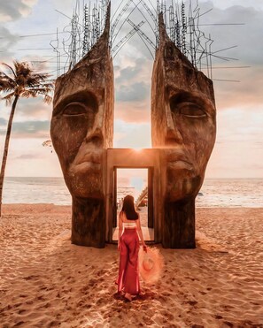 A woman standing in front of a large, abstract sculpture on a beach with a view of the ocean. - Sunset Sanato Resort & Villas (Phu Quoc)