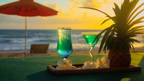 A tropical drink tray with a pineapple and flowers on a beach with an umbrella and ocean view. - Sunset Sanato Resort & Villas (Phu Quoc)