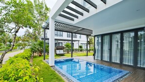 A modern outdoor pool area with a clear blue pool, surrounded by lush greenery and a covered seating area. - Sunset Sanato Resort & Villas (Phu Quoc)