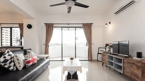 A modern living room with a black leather sofa, a white coffee table, a TV on a wooden cabinet, and a large window with curtains. - Desa Kiara Cozy Condo by SYNC (Kuala Lumpur)