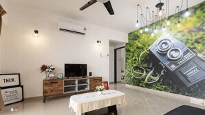 A modern living room with a flat-screen TV, wooden cabinet, and a table with a white tablecloth. - Desa Kiara Cozy Condo by SYNC (Kuala Lumpur)