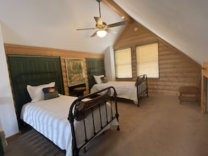 Une chambre dans un chalet en rondins, avec deux lits, un ventilateur de plafond et un tableau accroché au mur.