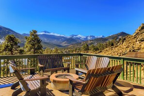 A deck with Adirondack chairs and a fire pit, overlooking a mountainous landscape.