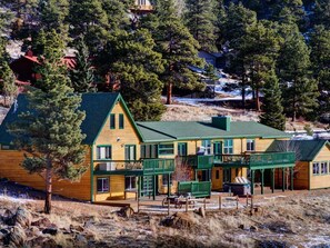 Eine zweistöckige Lodge mit grüner Dachdeckung und Holzverkleidung, umgeben von Bäumen und einem verschneiten Hügel.