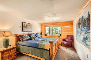 Ein gemütliches Zimmer mit einem Holzbett, einem Sessel, einem Gemälde und einem Fenster mit Blick auf Bäume.