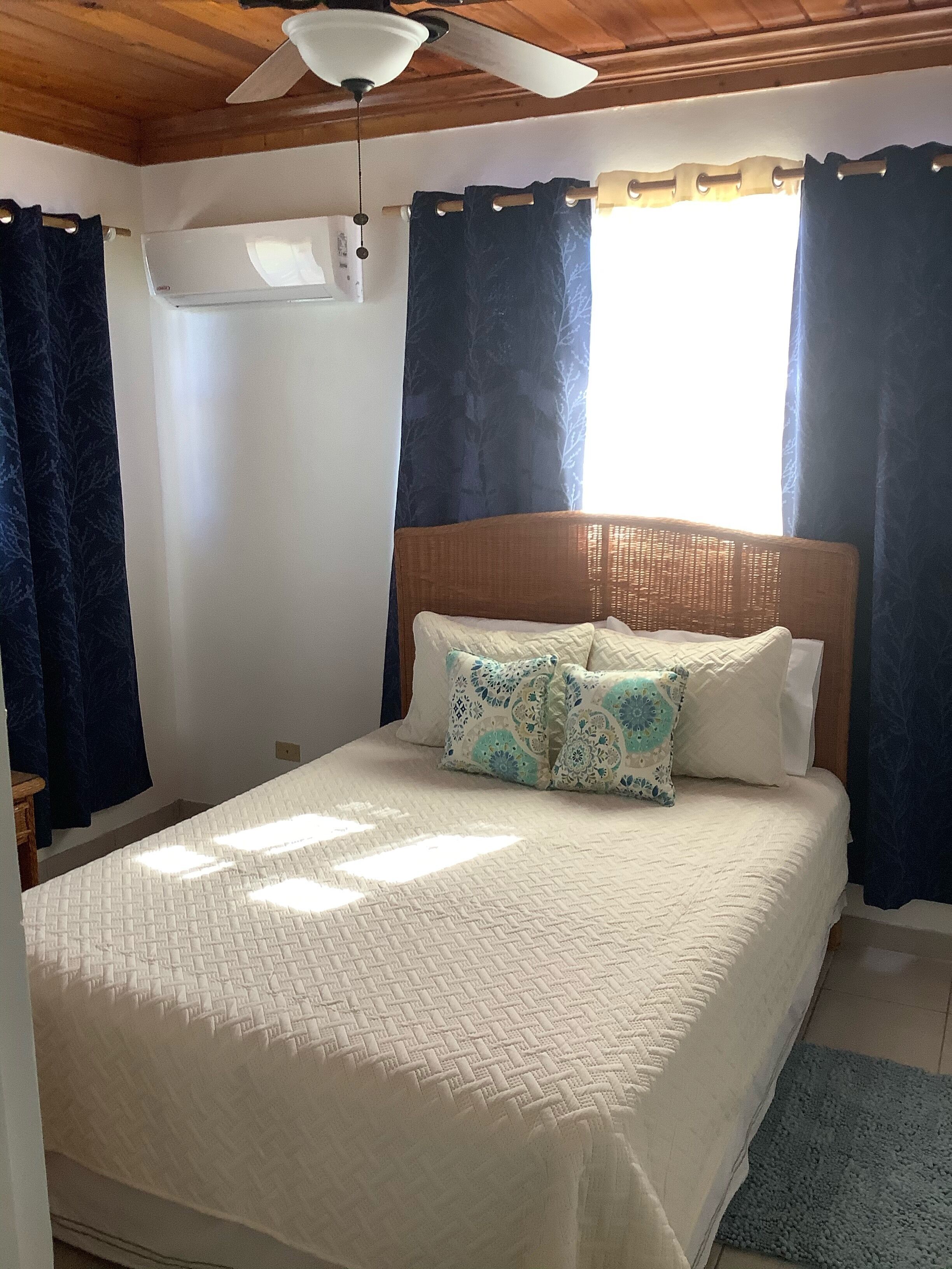 A bedroom with a bed, a ceiling fan, and a window with curtains.