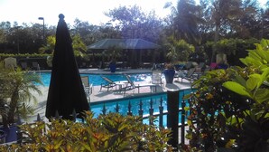 Ein Swimmingpool mit Liegestühlen und einer überdachten Liegefläche, umgeben von viel Grün.