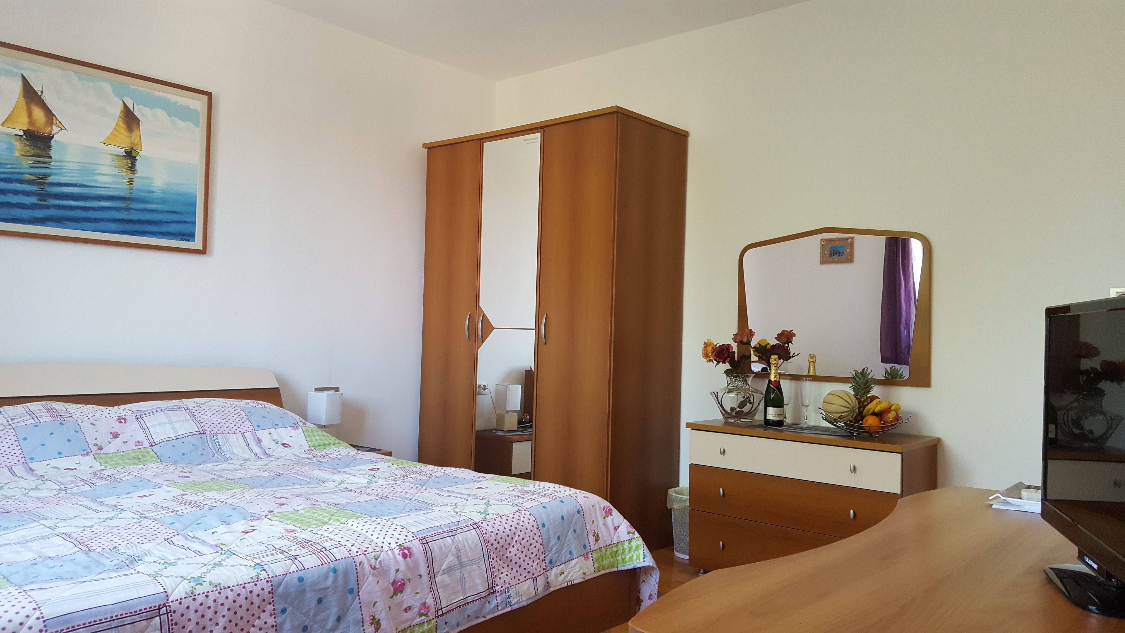 Un dormitorio con una cama, un armario de madera, un escritorio con espejo y un cuadro de veleros.