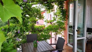 Un patio con una mesa y sillas, rodeado de follaje y un ventanal.