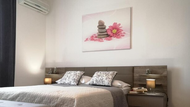 Un dormitorio con cama, lámparas de noche, mesita de noche y una obra de arte en la pared.