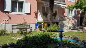 Un edificio residencial con balcón, escaleras y un jardín con un banco y una farola.