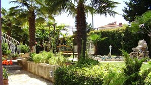 Un jardín con una escalera de piedra, palmeras y una fuente.