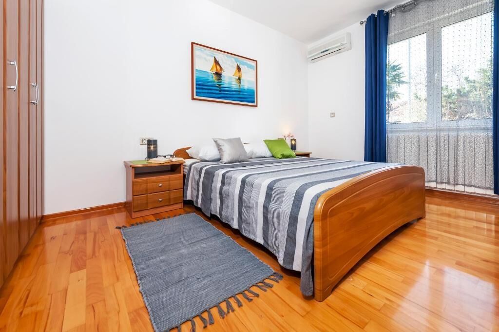 A bedroom with a wooden bed, a nightstand, a drawer unit, a gray rug, and a painting of sailboats on the wall.