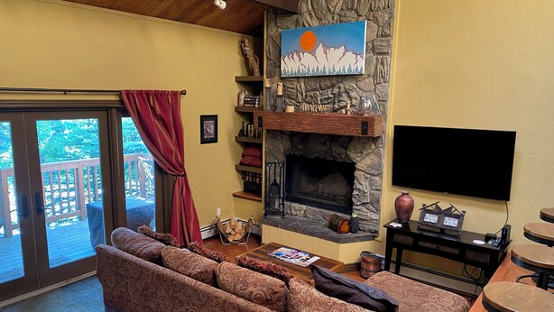 Una sala de estar acogedora con chimenea de piedra, un sofá grande y un televisor montado en la pared.