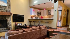 Una sala de estar moderna con un amplio sofá modular, un televisor de pantalla plana y una mesa de comedor con un cuenco decorativo.