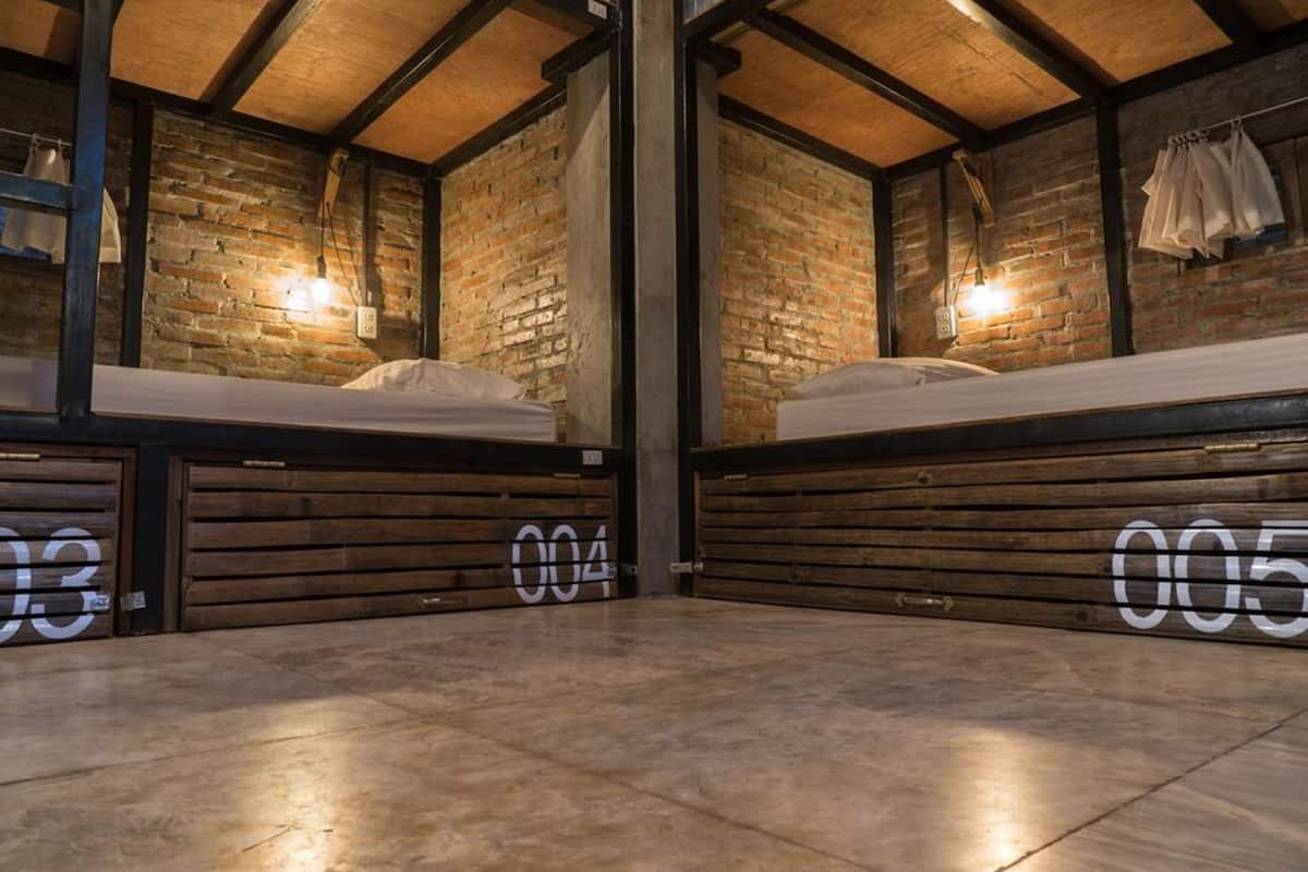 A room with two beds, wooden floors, brick walls, and exposed beams.