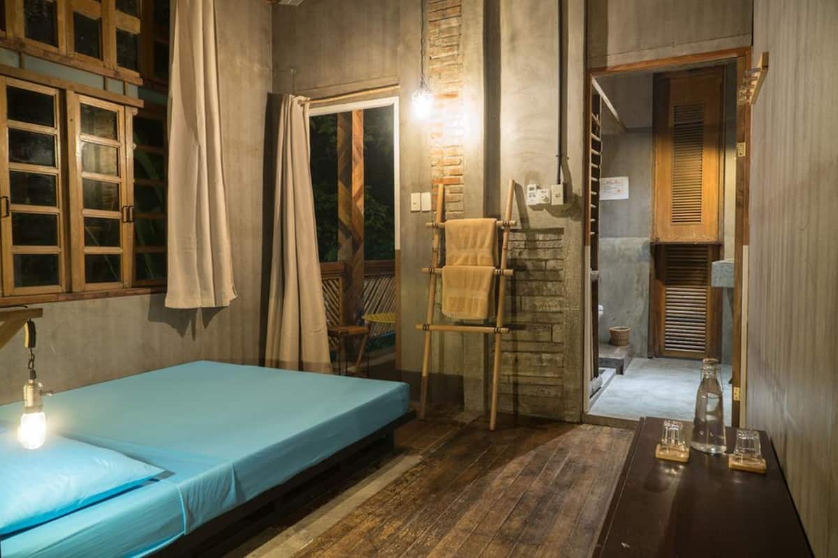 A room with a bed, a wooden ladder, a towel rack, and a small table with glasses and a bottle.