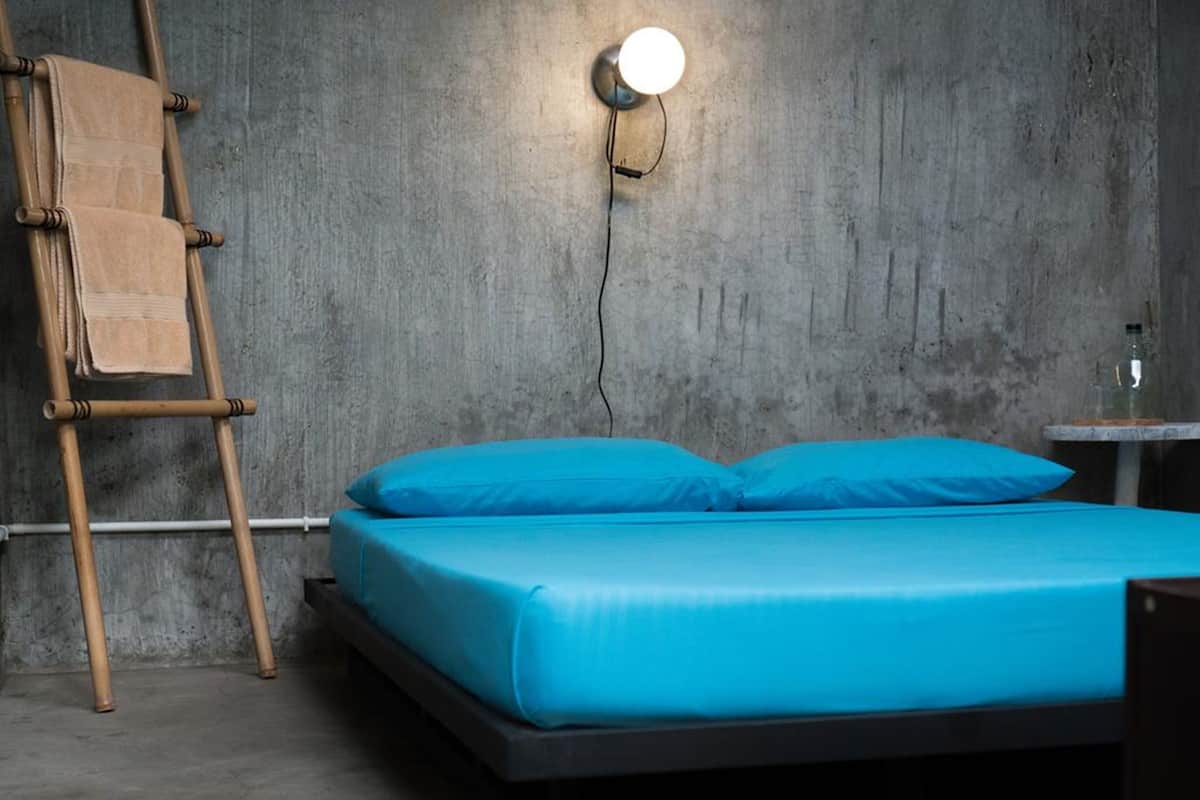 A bed with a blue mattress and pillows, a wooden ladder, and a wall-mounted light fixture.