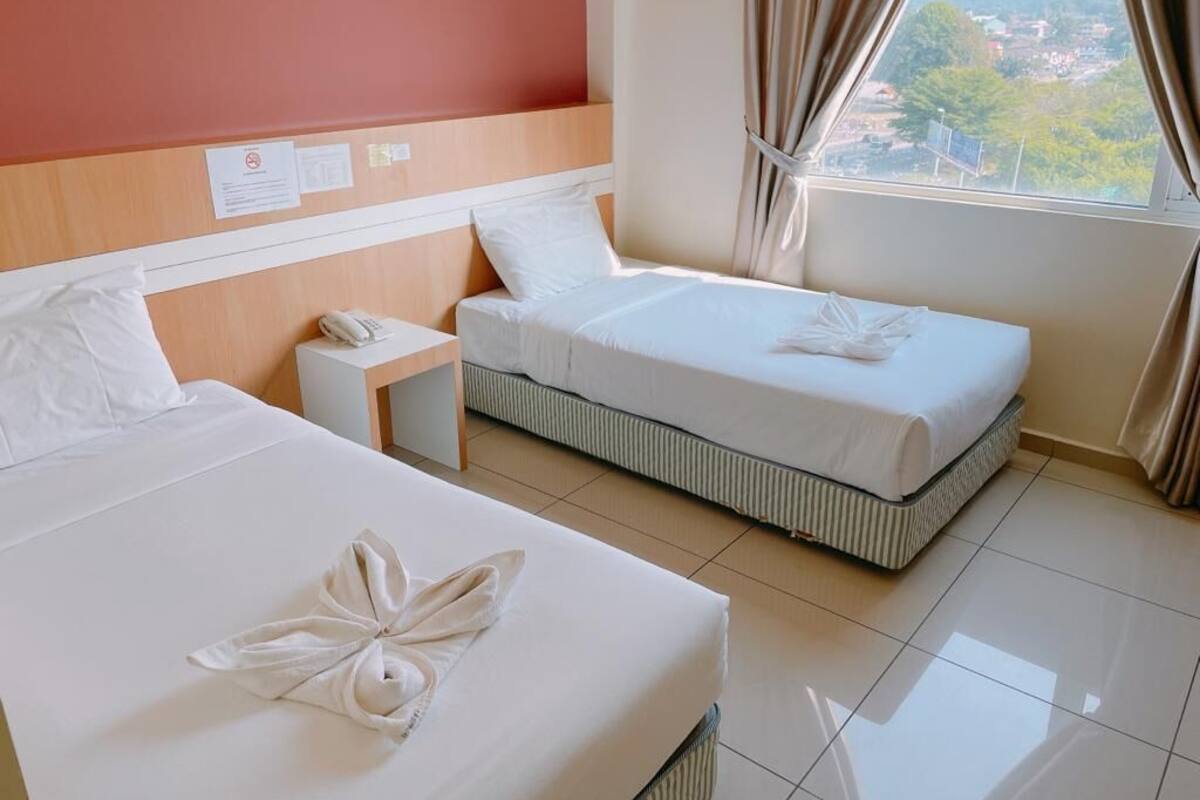 A hotel room with two beds, a nightstand, and a window with curtains.