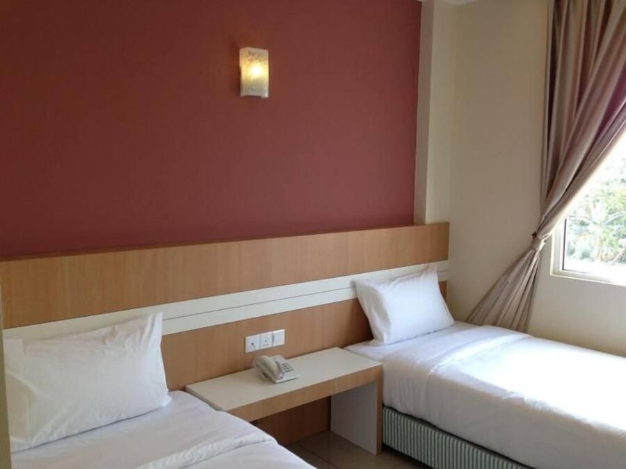 A hotel room with two beds, a bedside table with a phone, a wall-mounted light, and a window with curtains.