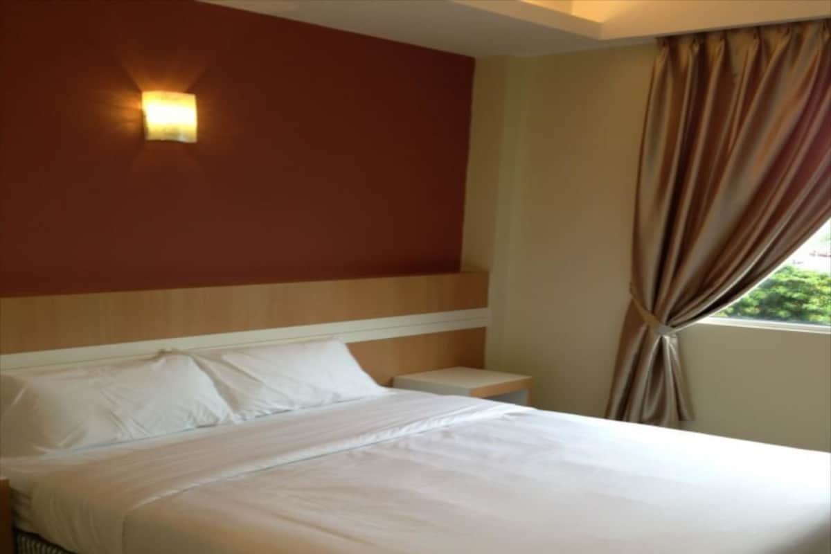 Habitación de hotel con cama, mesita de noche, lámpara de pared y ventana con cortinas.