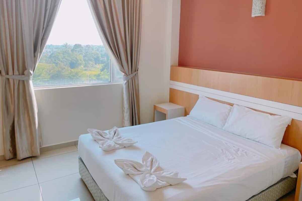A hotel room with a bed, curtains, a nightstand, and a view of greenery outside.
