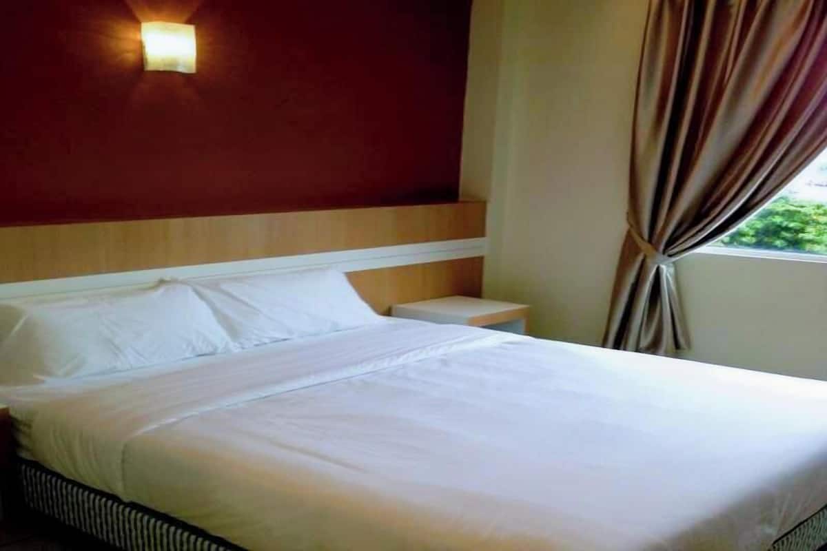 A hotel room with a bed, a nightstand, a wall-mounted light, and a window with curtains.