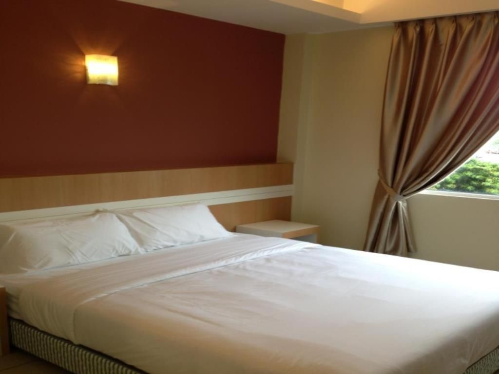 Een hotelkamer met een bed, nachtkastje, wandlamp en raam met gordijnen.