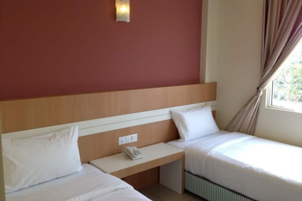 A hotel room with two beds, a bedside table with a phone, a wall-mounted light, and a window with curtains.