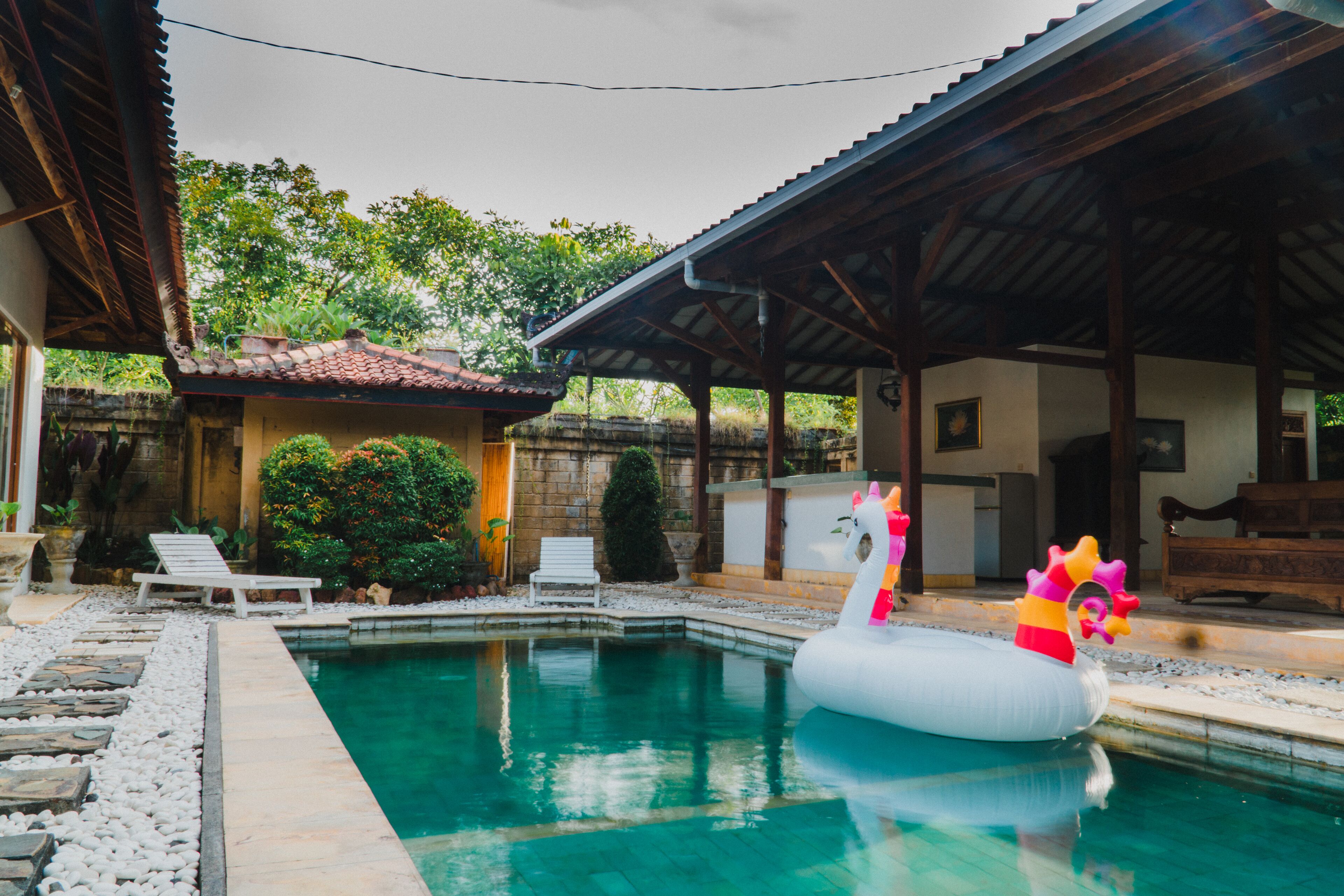 A swimming pool with an inflatable swan float, surrounded by stone tiles and white lounge chairs.