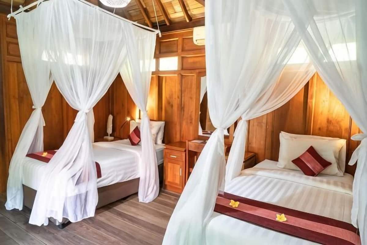 Une chambre avec deux lits, chacun doté d’un baldaquin, des murs en bois et une petite table de chevet avec une lampe.