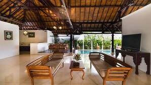 A spacious living area with wooden furniture, a pool view, and a TV. - Bali Royal Heritage Villas (Keroboken Kelod)