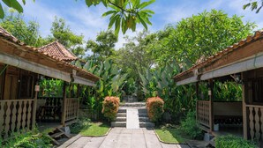 A courtyard with a central pathway leading to a staircase, surrounded by lush greenery and traditional wooden structures with tiled roofs. - Bali Royal Heritage Villas (Keroboken Kelod)