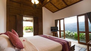 A bedroom with a large bed, a television, and a view of the ocean. - Bali Royal Heritage Villas (Keroboken Kelod)