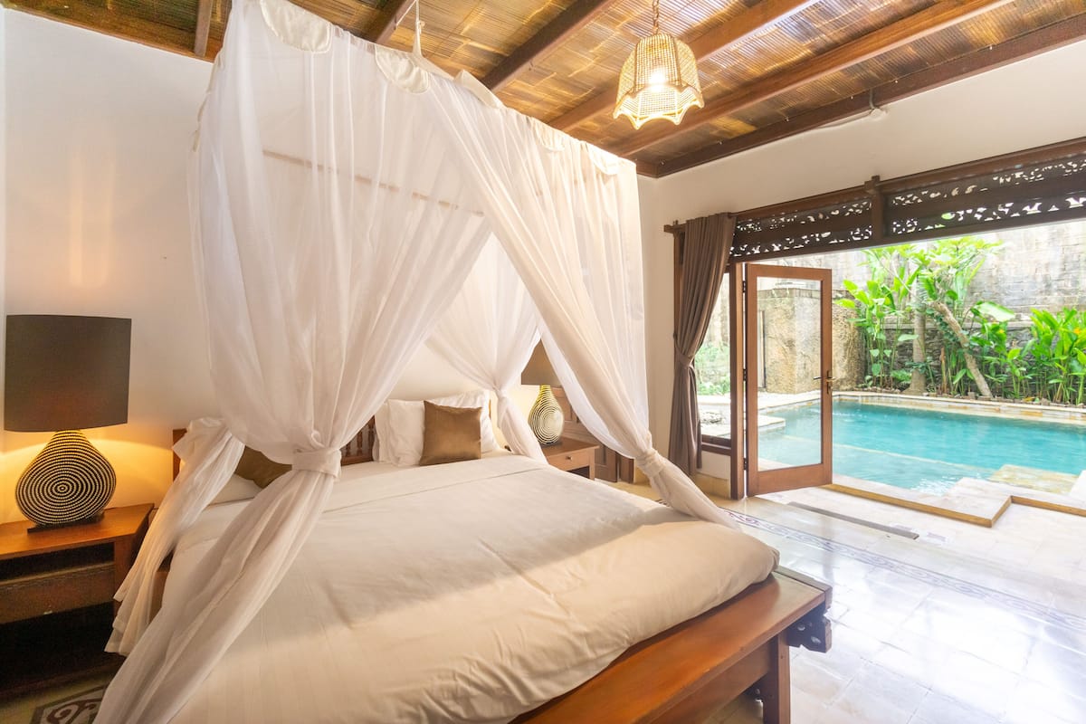 Une chambre à coucher avec un lit à baldaquin, une lampe de chevet et une vue sur une piscine.