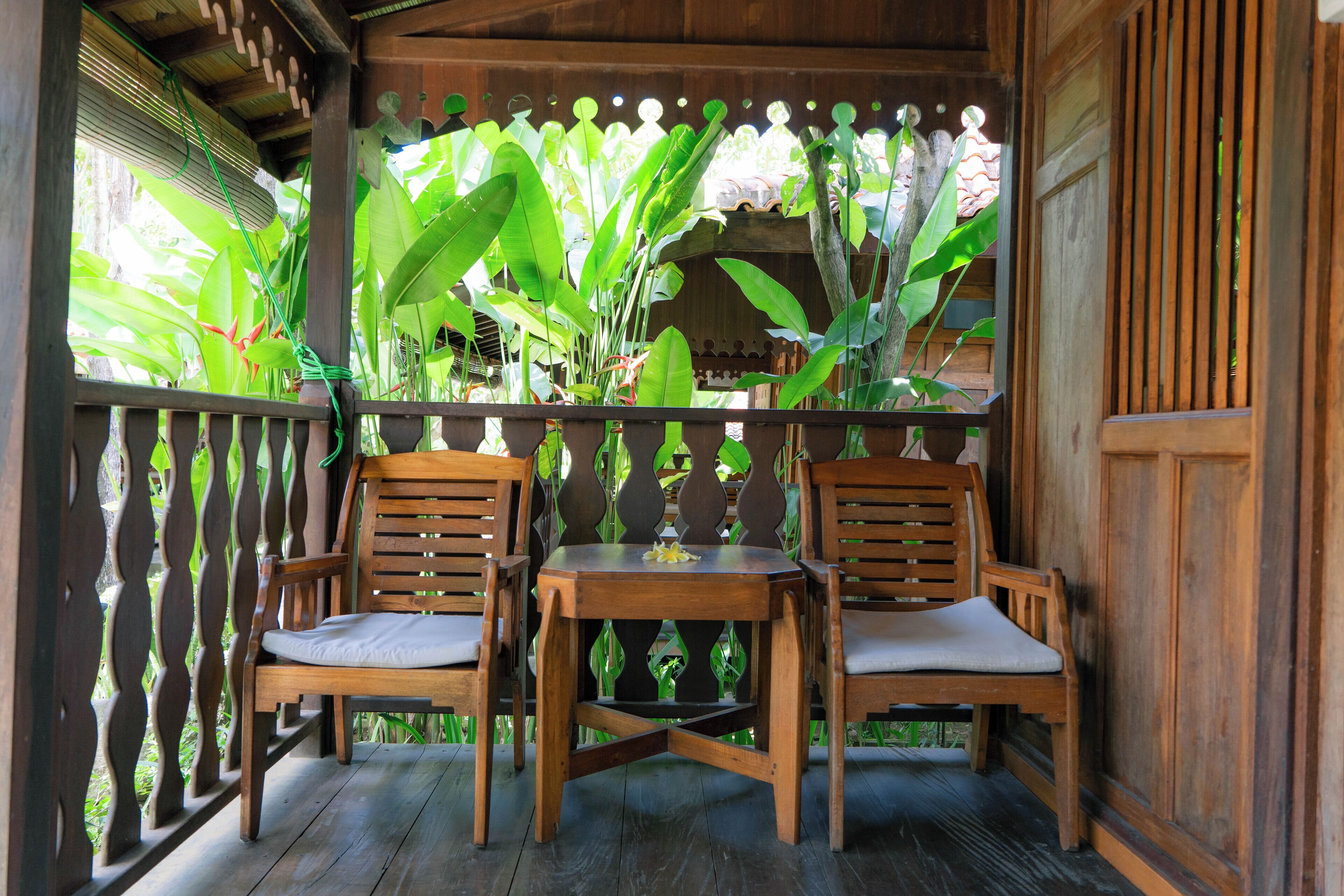 Une terrasse en bois avec deux chaises et une table, entourée d’une végétation luxuriante.