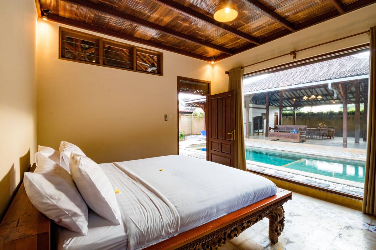 Une chambre avec un lit en bois et une grande fenêtre donnant sur une piscine.
