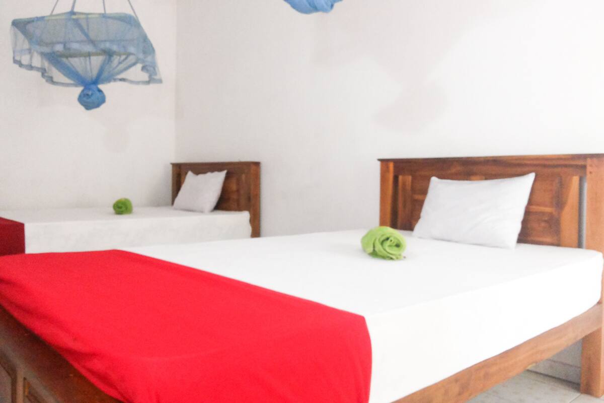 A hotel room with two beds, one with a red blanket and the other with a green towel.
