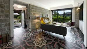 A room with a patterned floor, a black sofa, a stone wall, and a large window with a view. - Appart'sHotel Fior Di Ribba (Sartene)